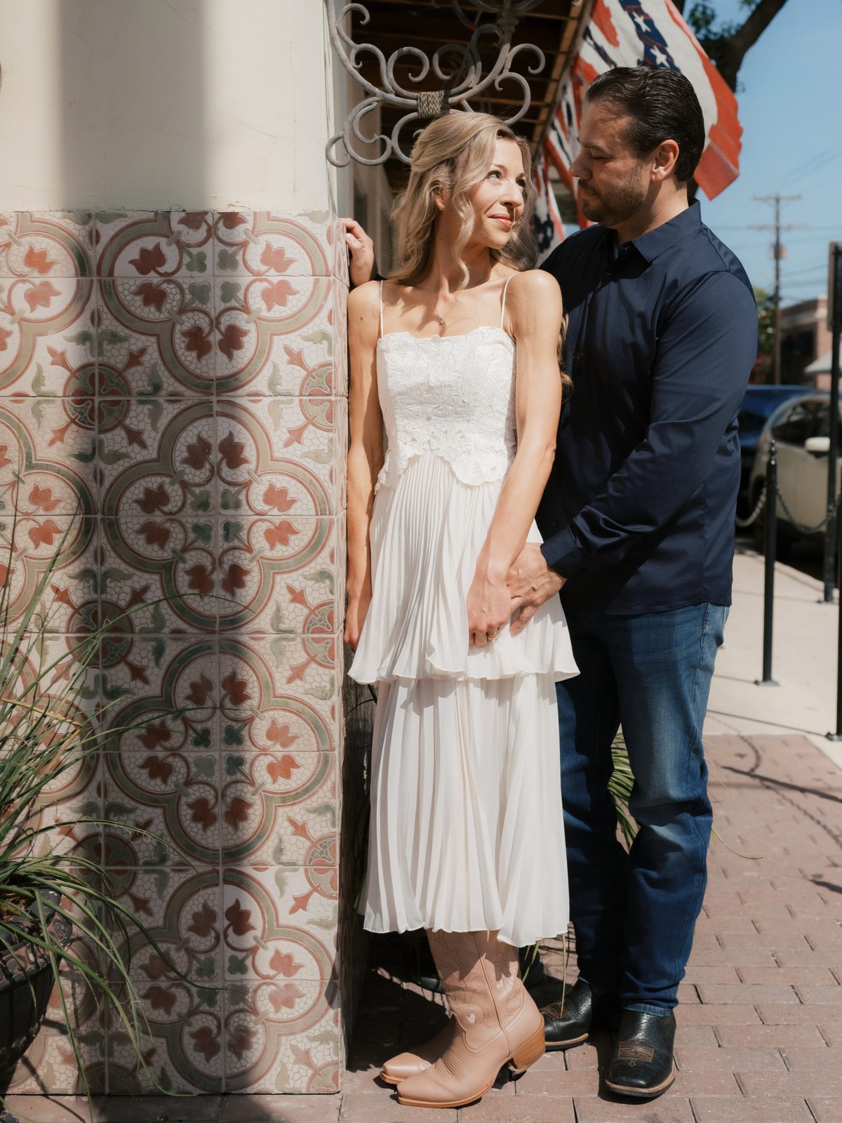 Chris and Brittney holding hands beside a patterned tile wall